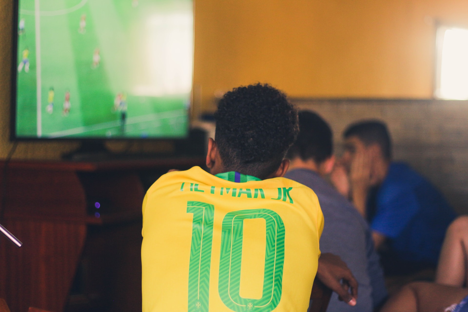 man wearing brazil shirt while watching football on tv